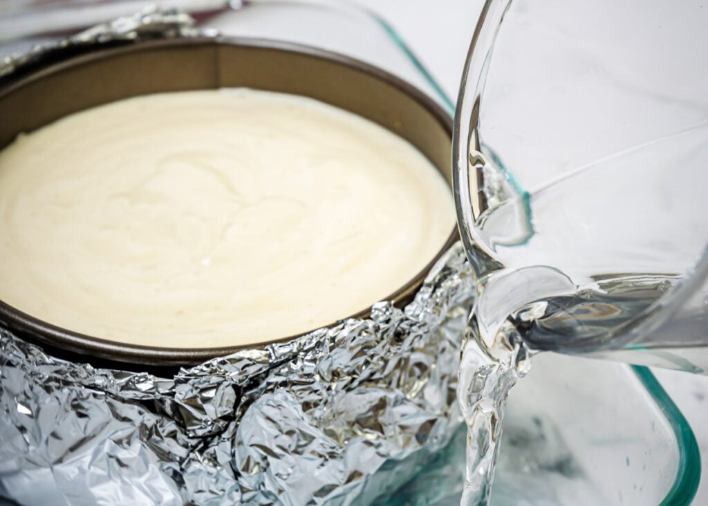 Pouring water into baking pan for cheesecake water bath.