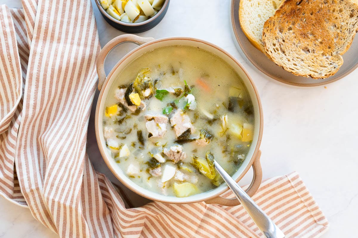 Full of green borscht with chopped hard-boiled eggs and bread for serving.