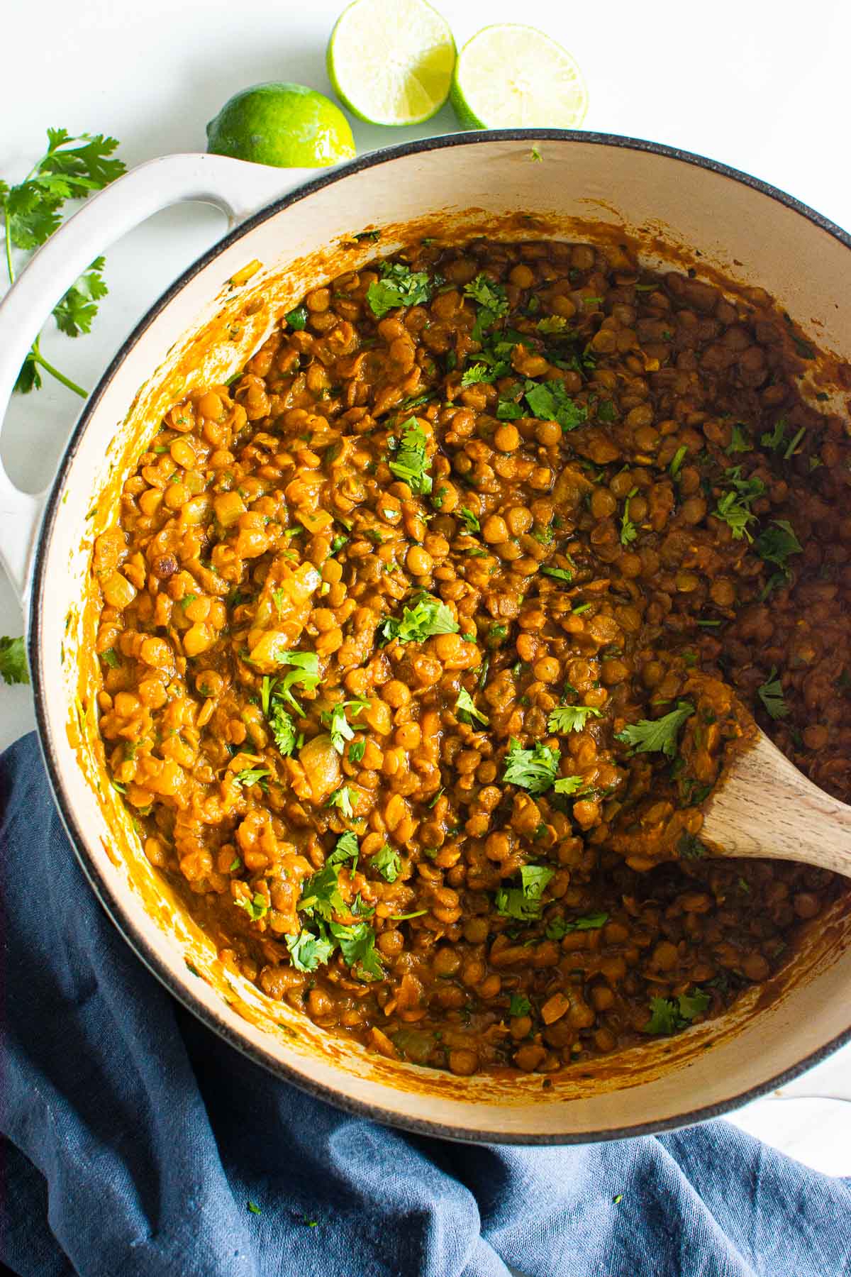 Green lentil curry garnished with cilantro in a pot with wooden spoon.