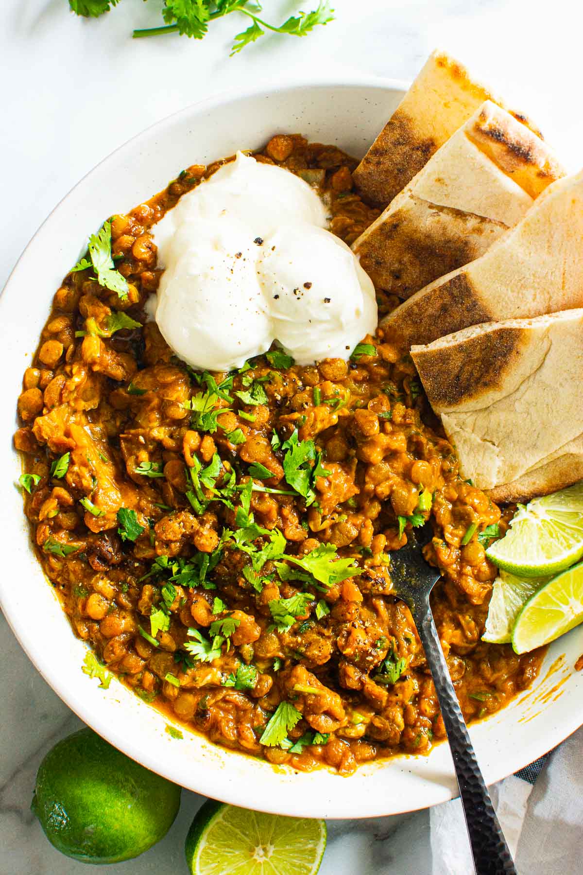 Green lentil curry with lime, pita, cilantro and sour cream served in a bowl with a fork.