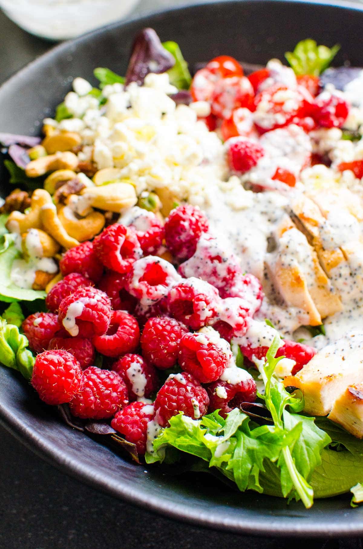 Grilled chicken salad with dressing and fruits and nuts in black bowl.