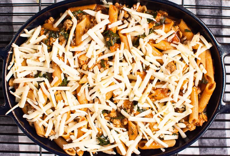Cheese over a dish of pasta with kale and ground turkey.