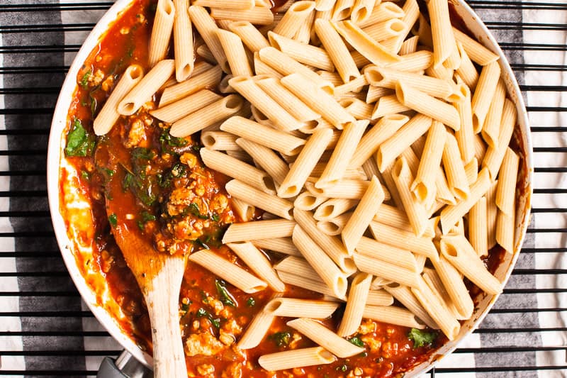 Pasta being added to ground turkey, kale and red sauce.
