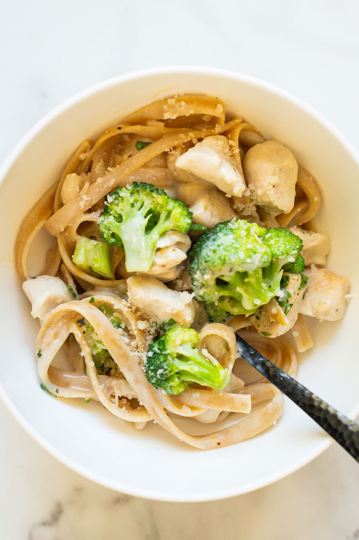Fettuccine chicken alfredo garnished with Parmesan cheese in a bowl with a fork.