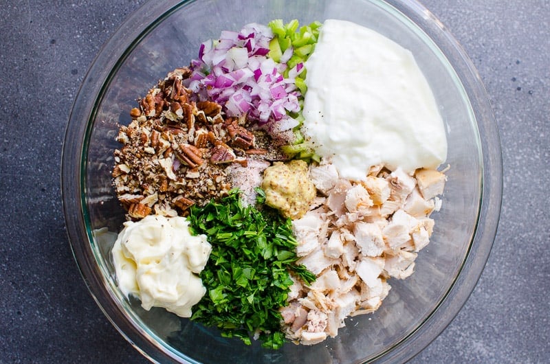 Pecans, greek yogurt, mayo, cooked chicken, red onion, mustard, celery and fresh herbs in glass bowl. 