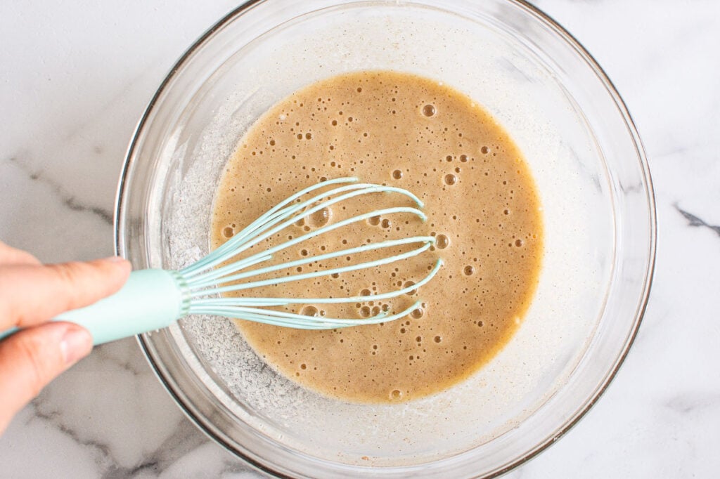 Person whisking liquid ingredients in a glass bowl.