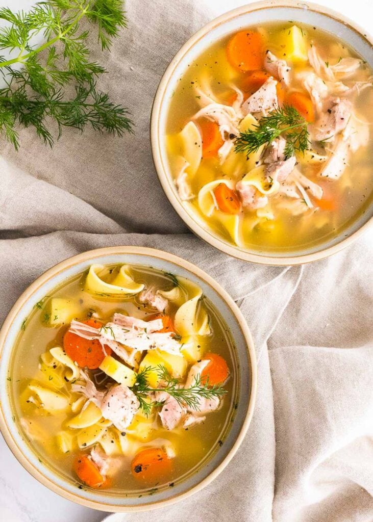 Two bowls with chicken, noodles and carrots with dill garnish. 