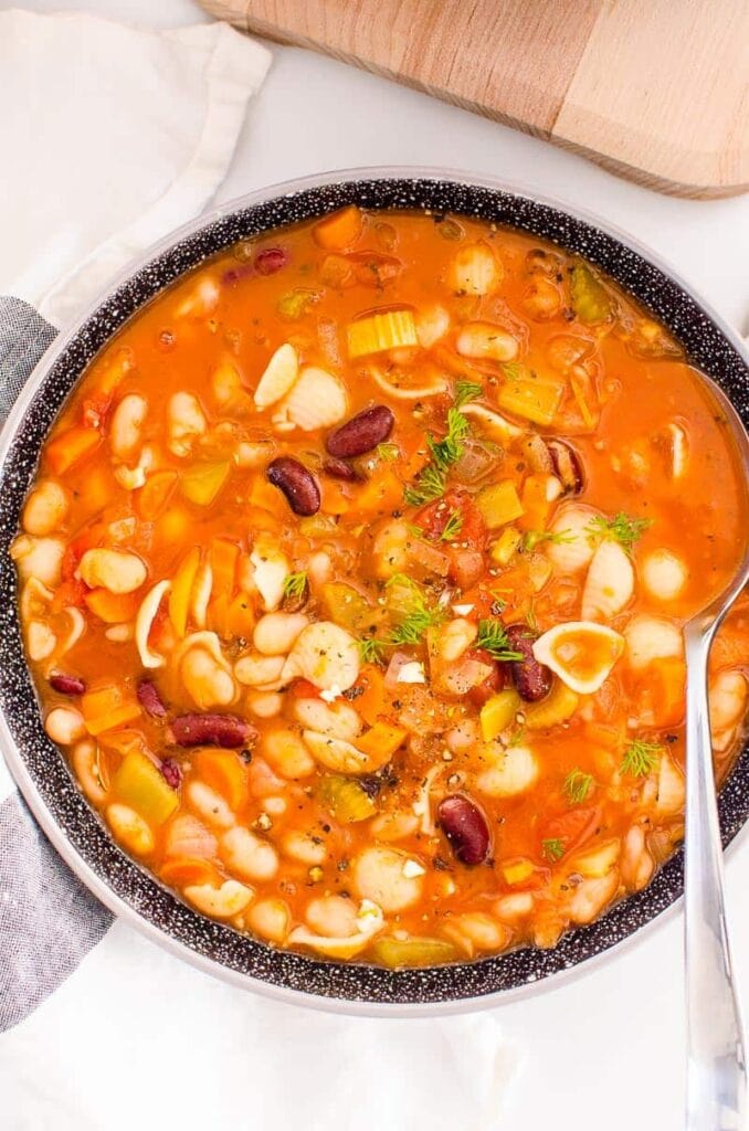 Pasta shells with red beans and vegetables in bowl with spoon.