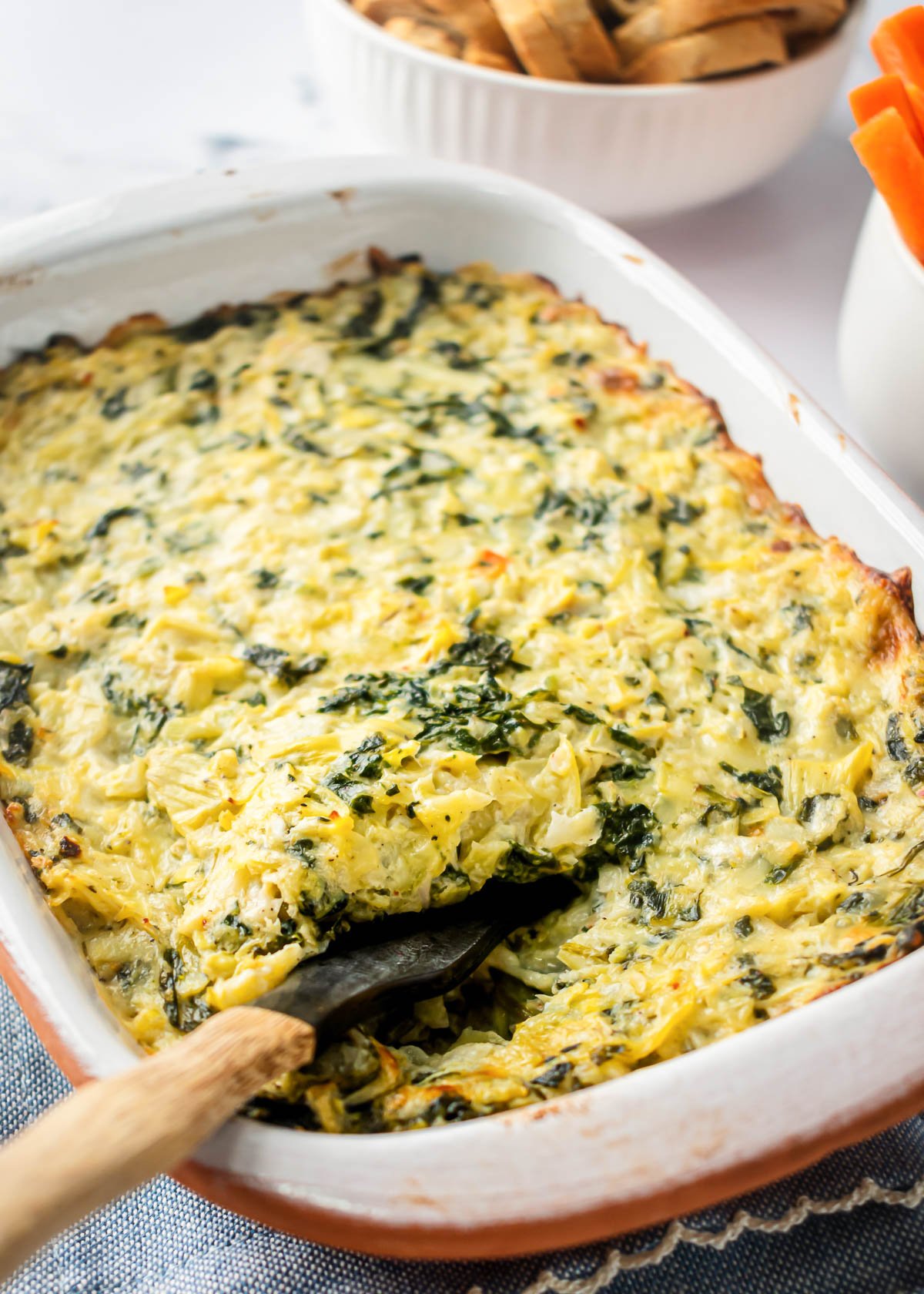 Healthy spinach artichoke dip in baking dish with a spoon.