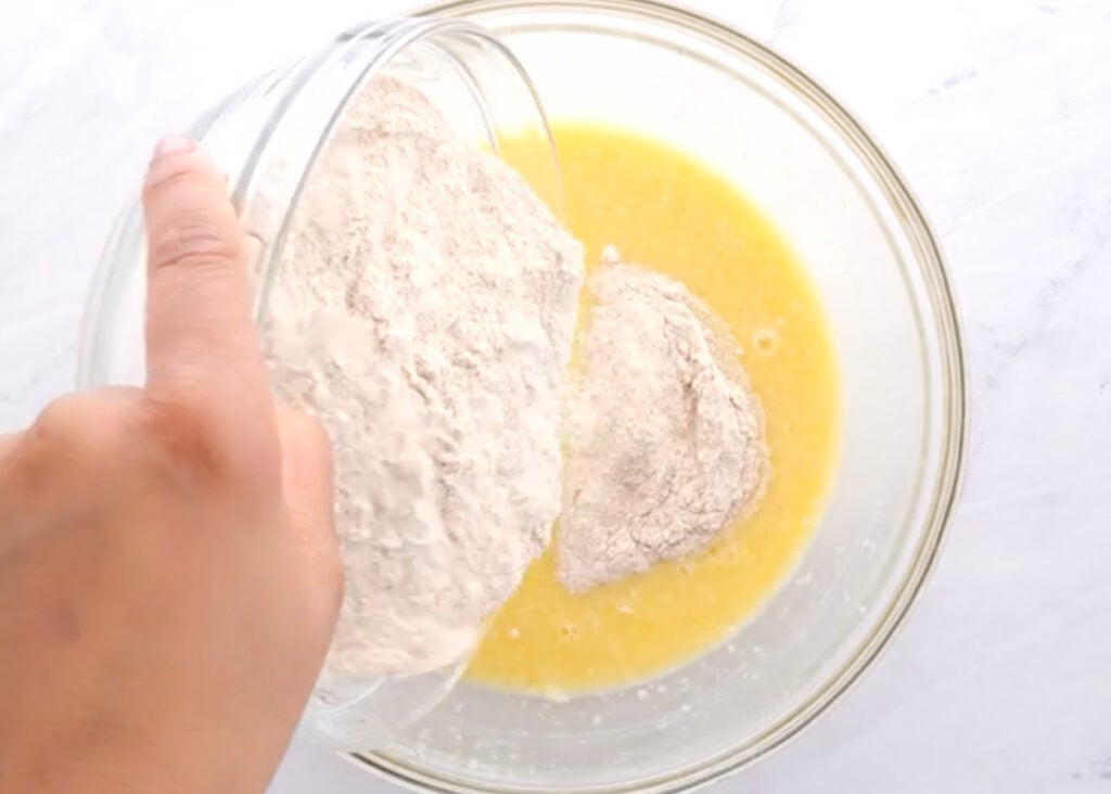 Adding flour to egg mixture for a waffles batter.