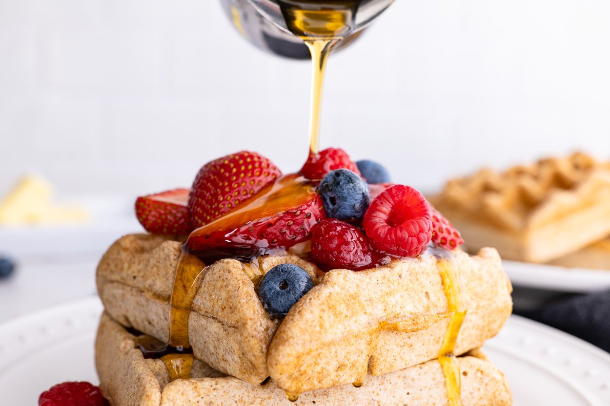 Pouring maple syrup on a stack of healthy waffles topped with fresh berries.