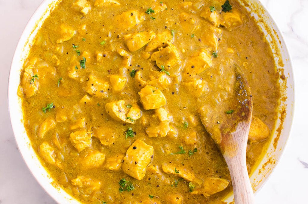 Yellow chicken curry stirred with wooden spoon and cilantro garnish.
