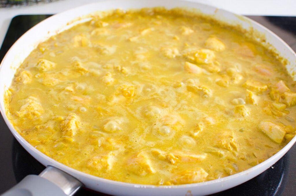 Simmering yellow chicken curry in skillet.