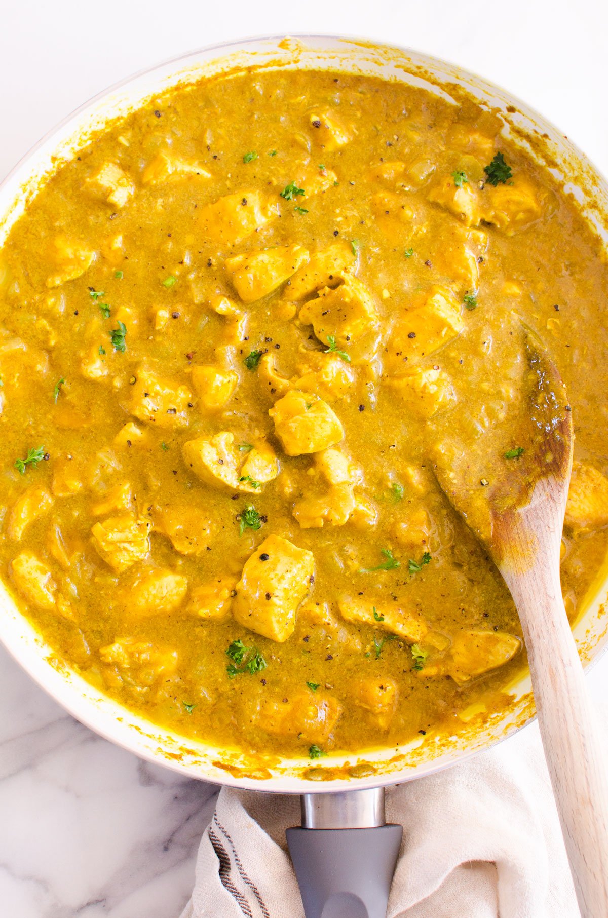 Chicken curry in skillet with garnish and wooden spoon.