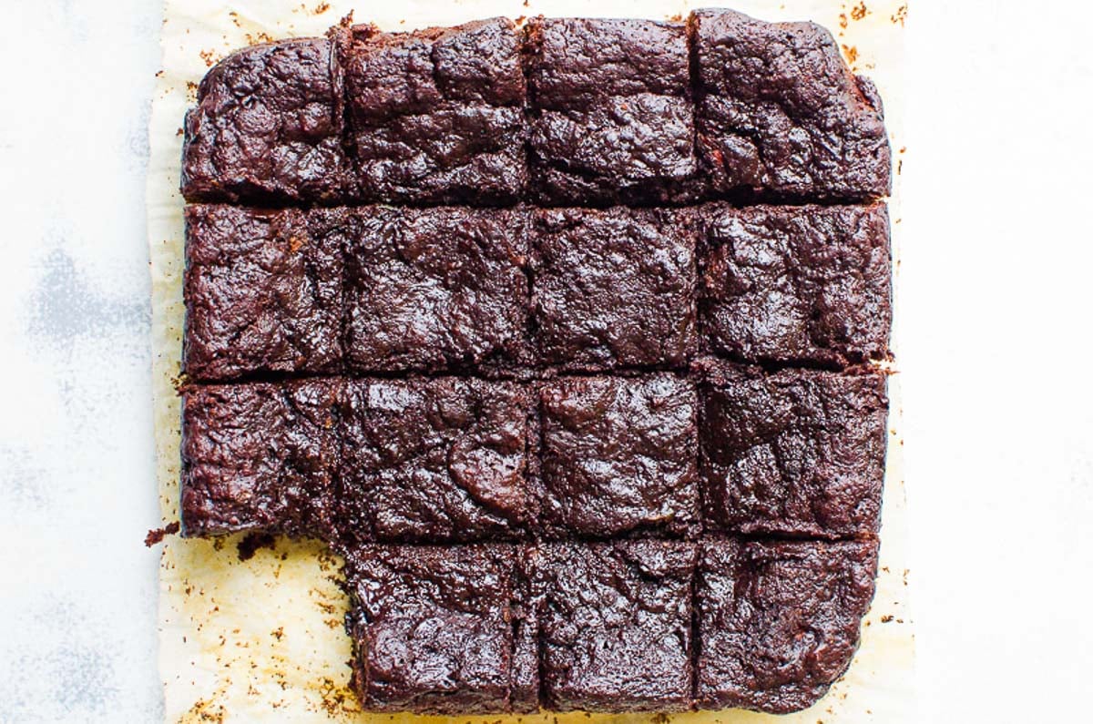 Zucchini brownies cut into squares on the counter with one browning missing.