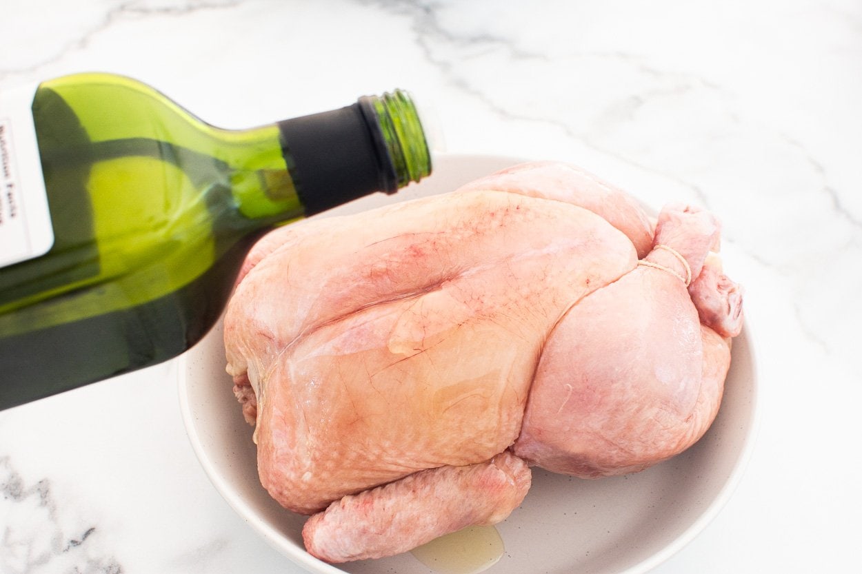 Avocado oil being poured onto whole chicken on a plate.