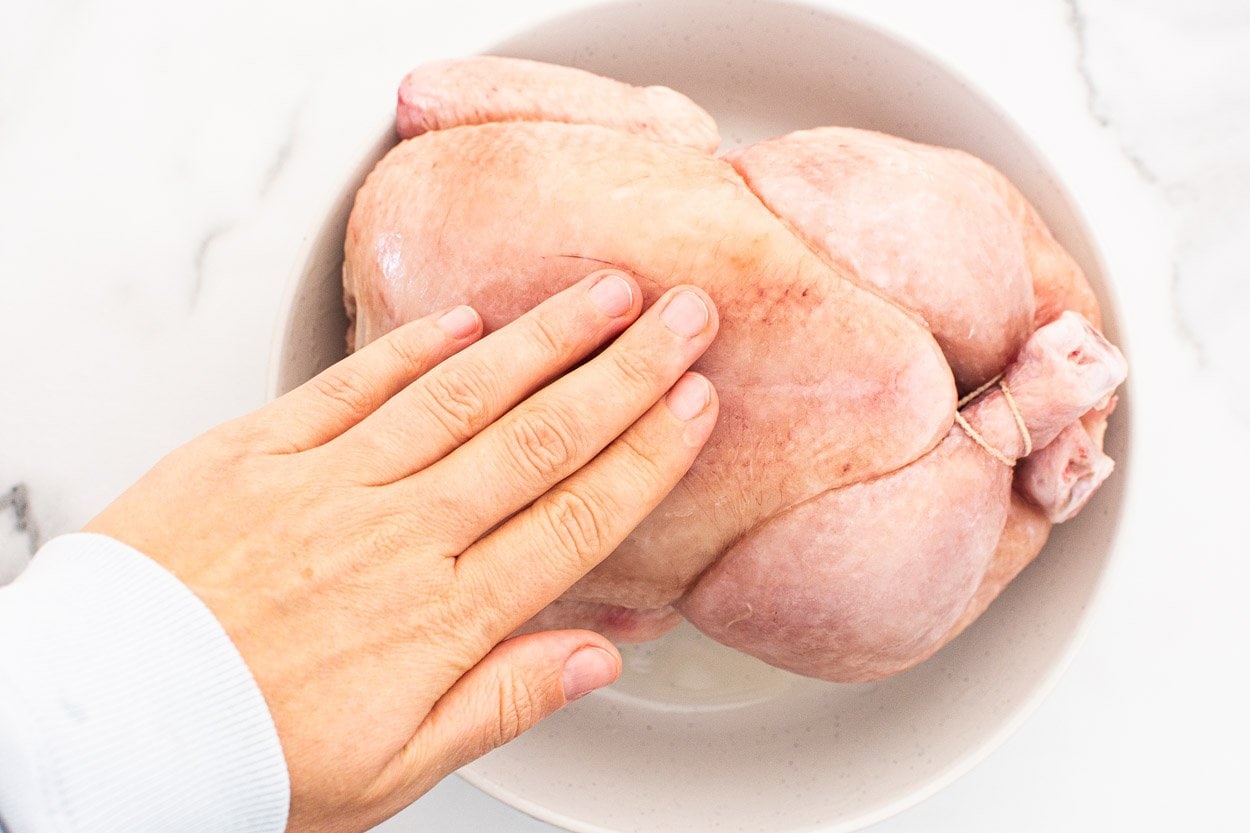 Person rubbing chicken with oil on a plate.