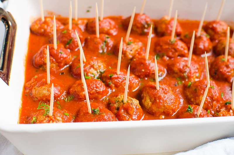Meatballs in sauce and garnished with parsley served with toothpicks in a baking dish.