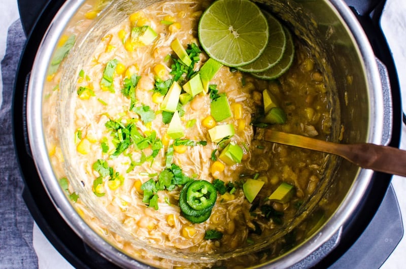 Chili in Instant Pot with a spoon, lime, chopped avocado and cilantro.