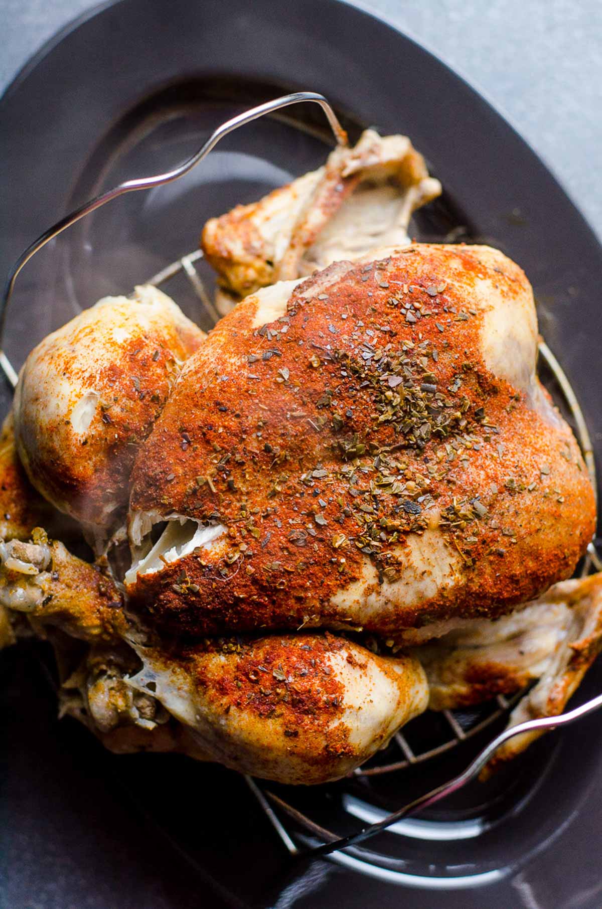 Cooked Instant Pot frozen whole chicken on a trivet on gray platter.