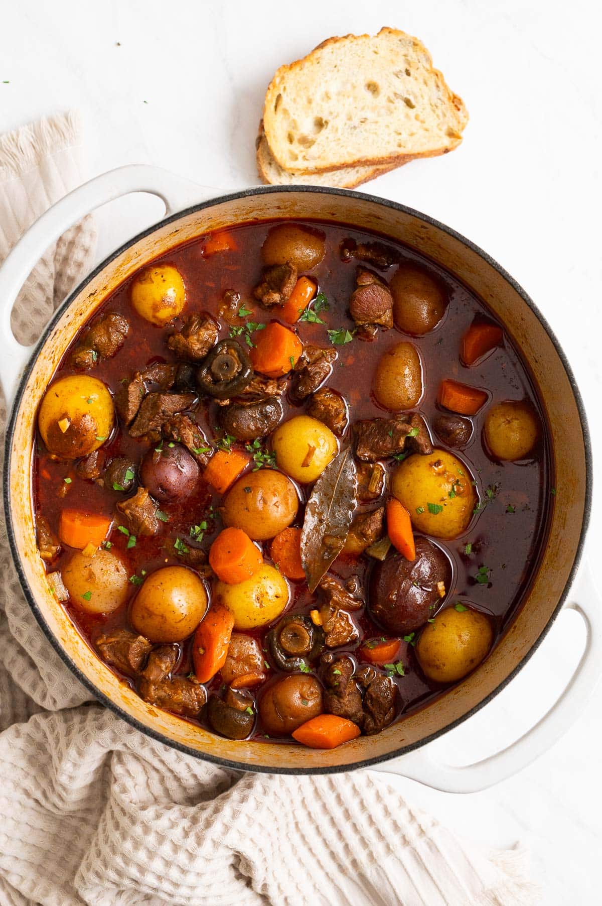Lamb stew with carrots, potatoes and mushrooms garnished with parsley in white pot.