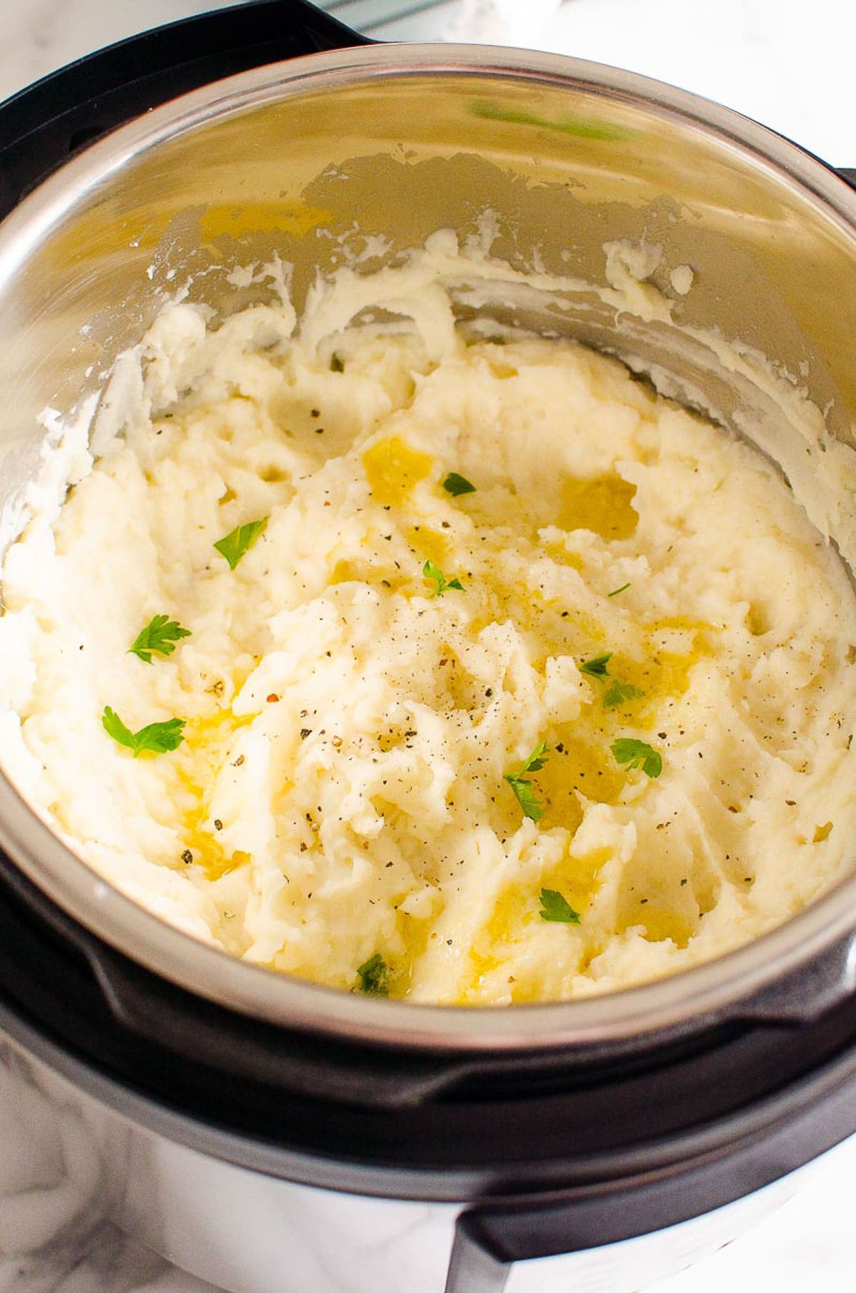 Mashed potatoes in Instant Pot garnished with parsley and pepper.