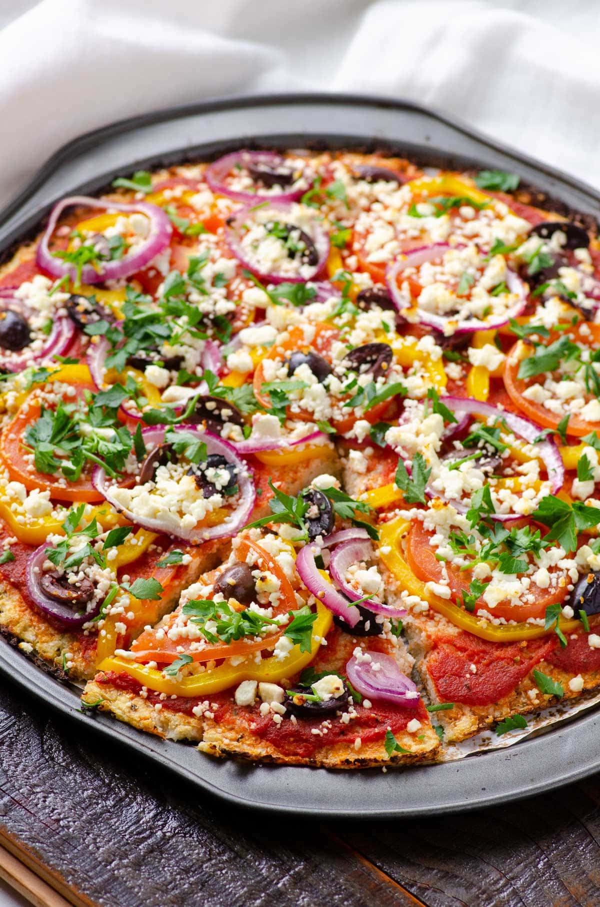 Mediterranean cauliflower pizza with bell peppers, olives, red onion and feta cheese.