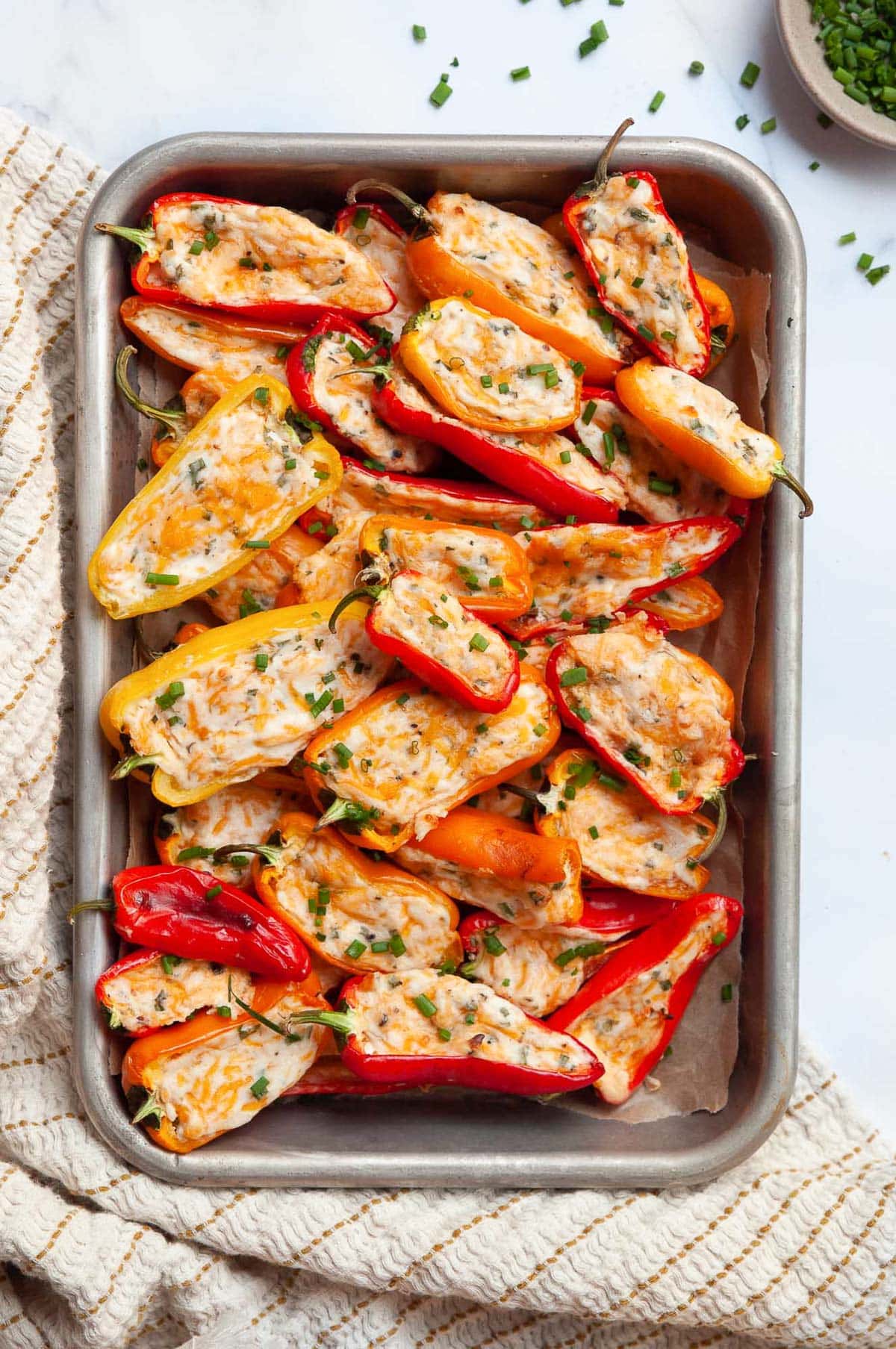 Stuffed with cream cheese mini sweet peppers garnished with chives and served on a metal tray.