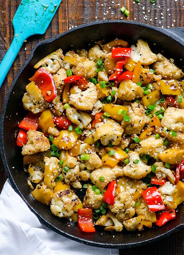 Cauliflower stir fry in cast iron skillet with blue spatula.