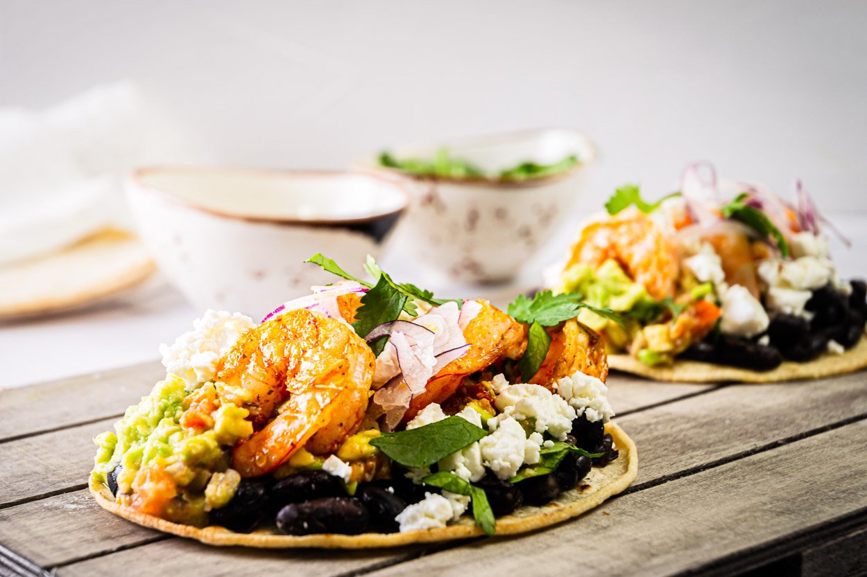 Tostadas layered with shrimp, black beans, guac, onion and cilantro.