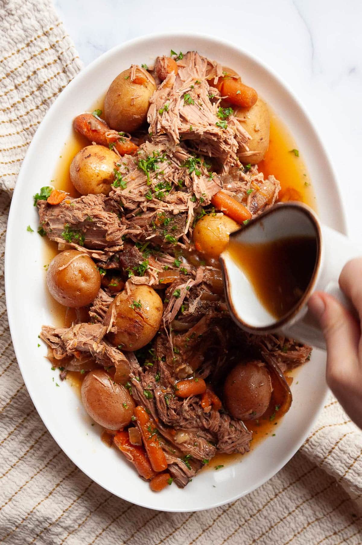 Person pouring gravy over cooked sirloin tip roast with veggies in slow cooker.