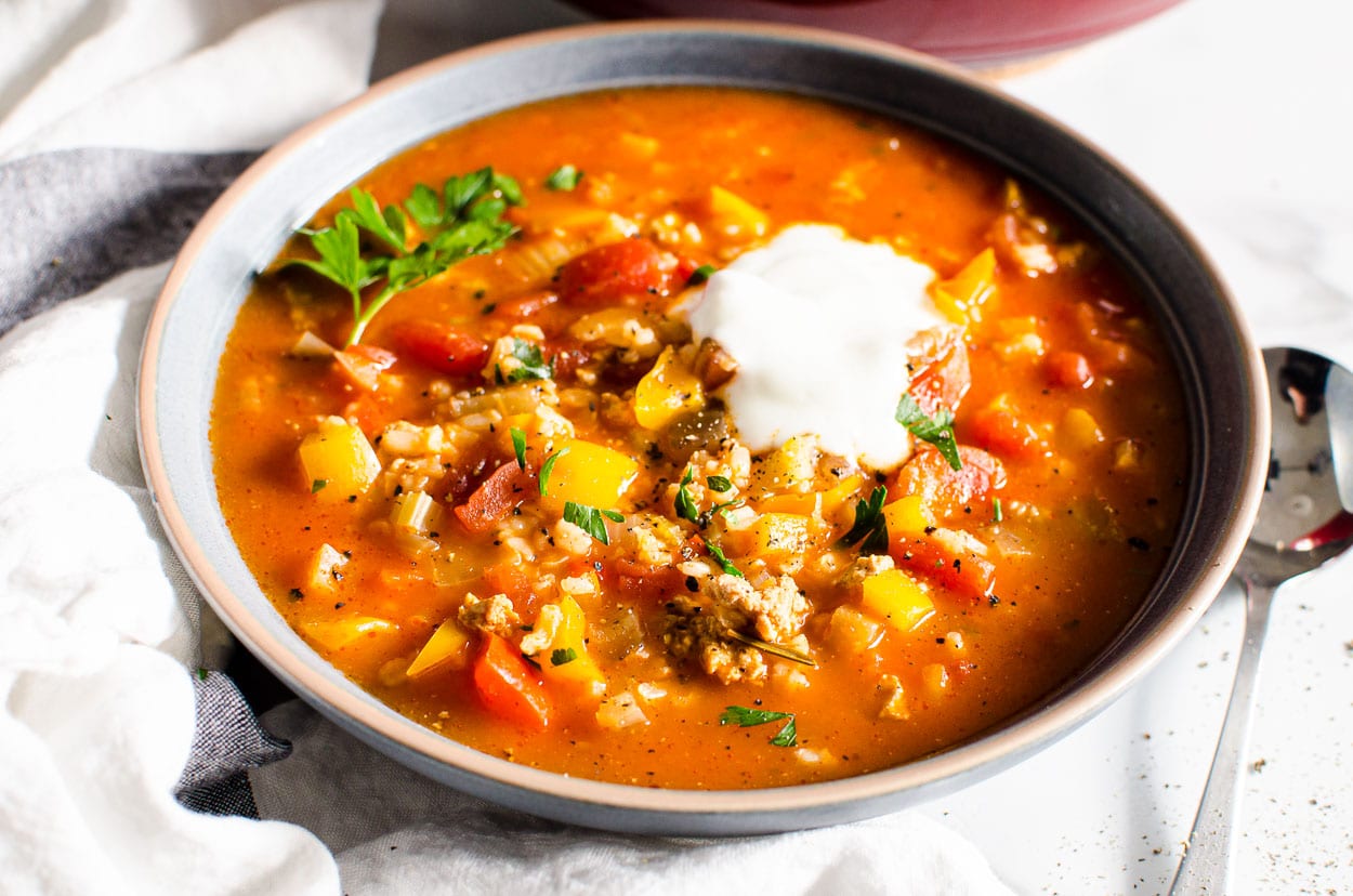 Stuffed pepper soup in bowl with spoon beside bowl and dollop of yogurt.