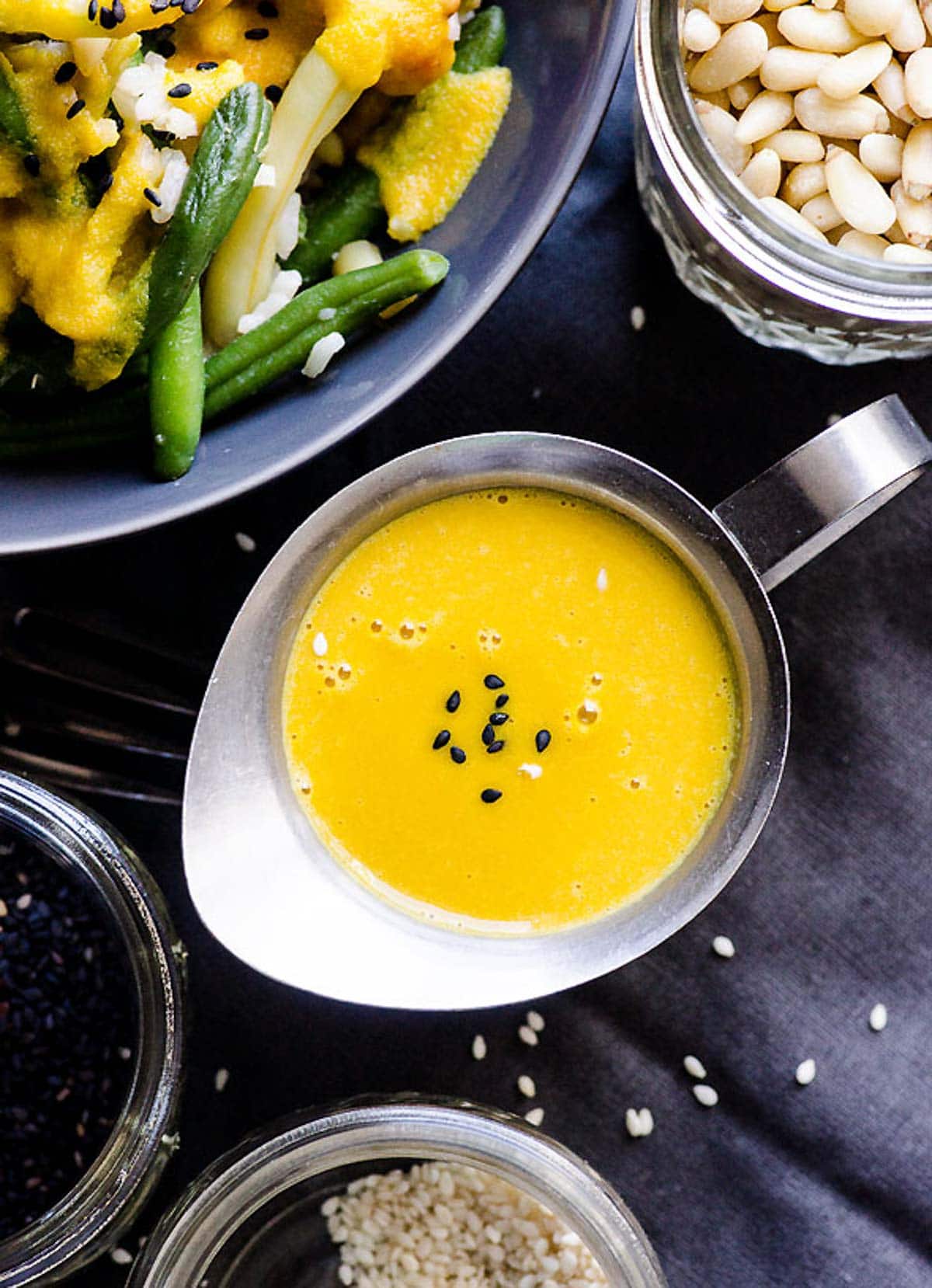 Carrot ginger salad dressing in a small silver serving dish with stir fry in bowl.