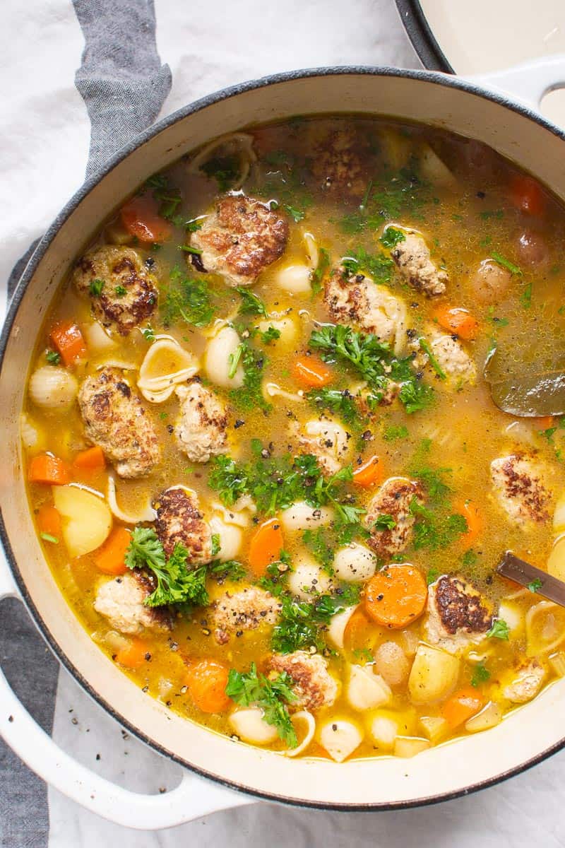 Turkey meatball soup garnished with parsley in white pot.