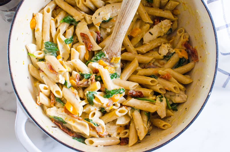 Tuscan chicken pasta with sun-dried tomatoes and spinach in a pot with wooden spoon.