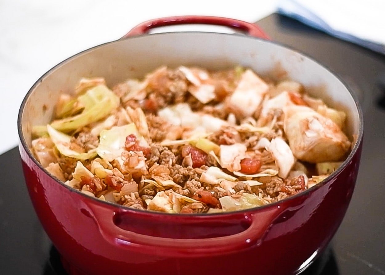 Stirred and uncooked unstuffed cabbage rolls in red pot.