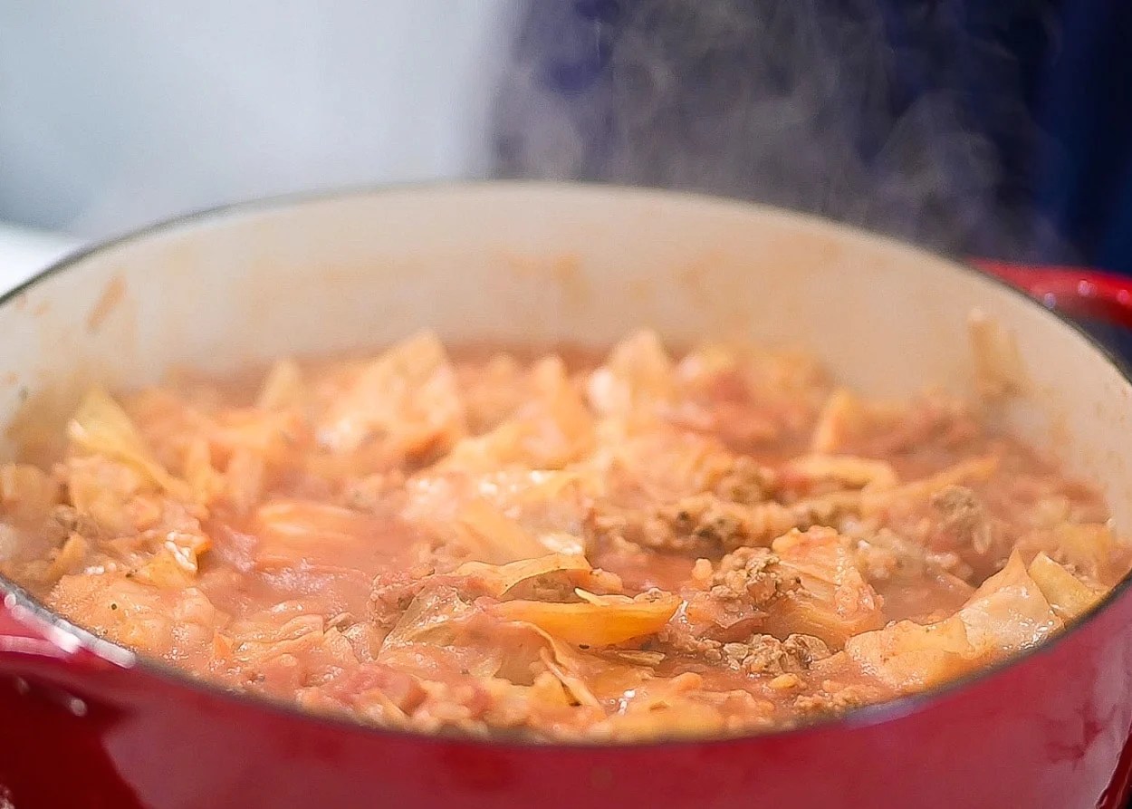 Cooked unstuffed cabbage rolls in red pot.
