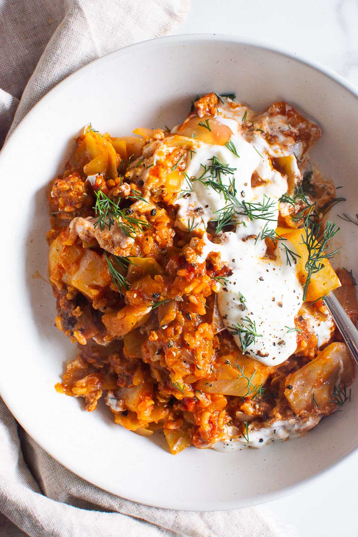 Unstuffed cabbage rolls with yogurt and dill in a serving bowl with a fork.