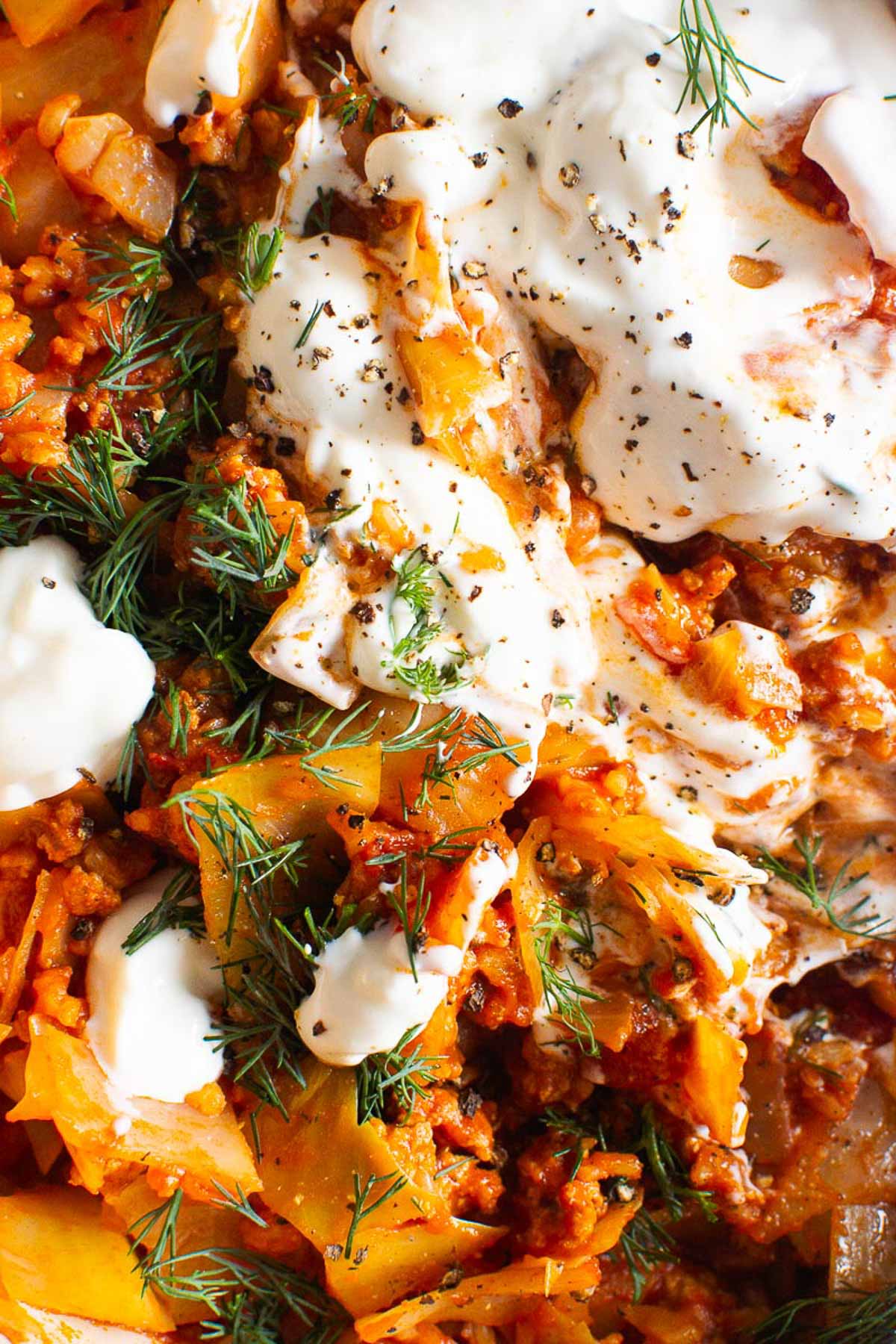 Close up of unstuffed cabbage rolls garnished with yogurt, dill and pepper.