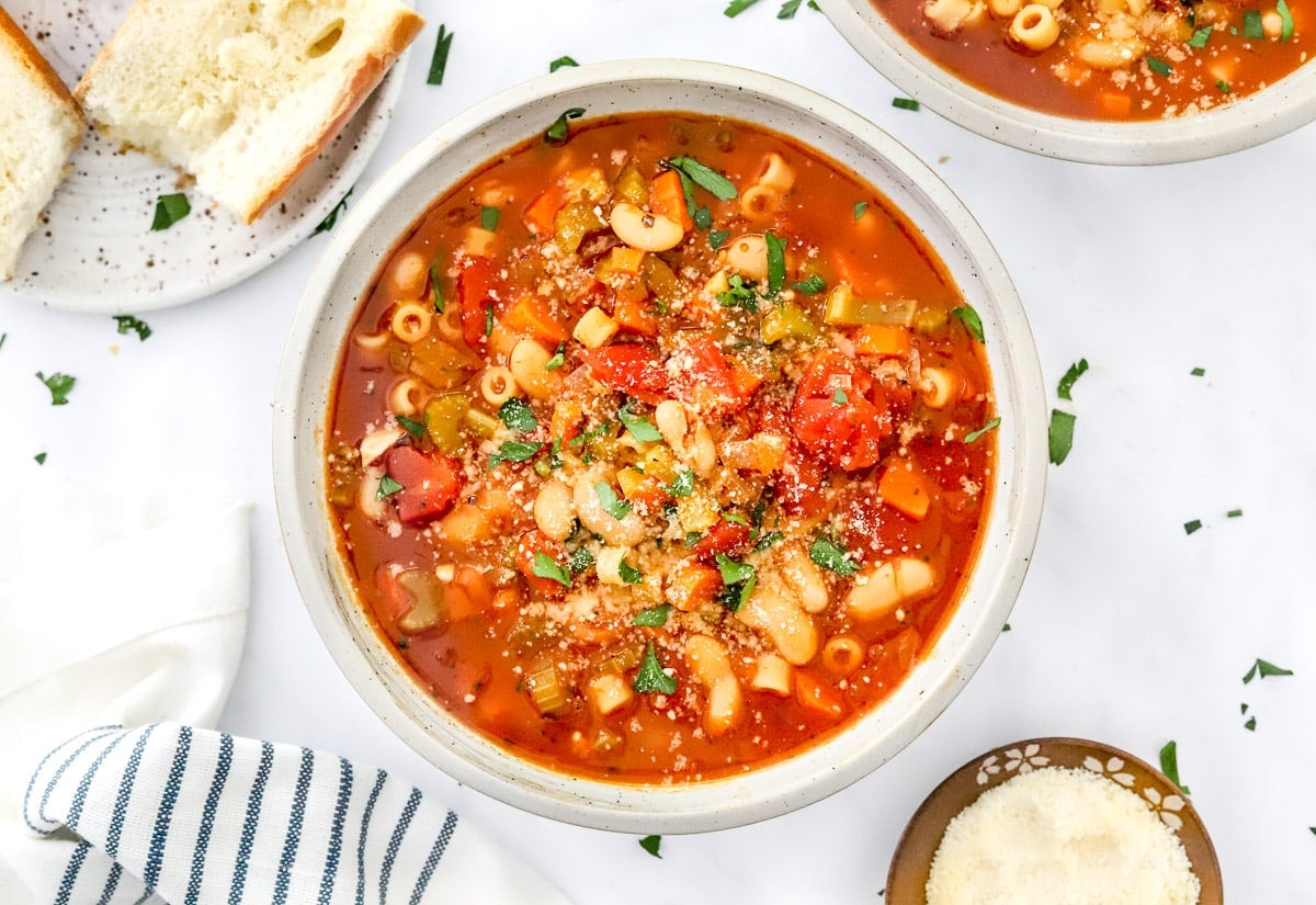 Vegetarian pasta fagioli garnished with Parmesan cheese and parsley in white bowl.