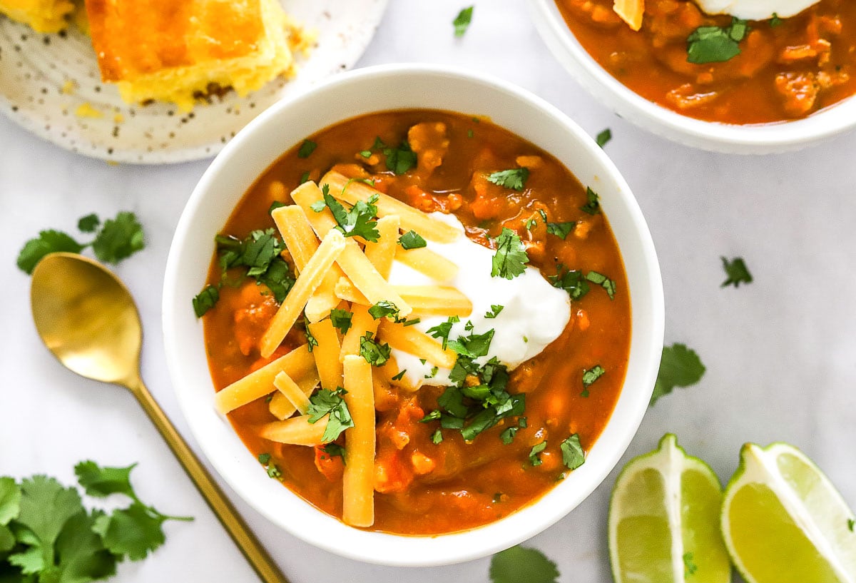 Pumpkin turkey chili with cheddar, sour cream and cilantro garnishes in a bowl.